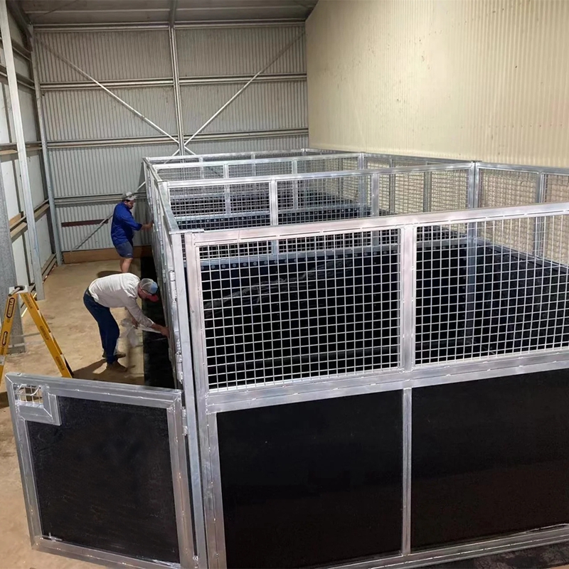 Two workers are installing the upper mesh front horse stall.