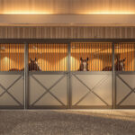 A sleek indoor horse stable with illuminated stalls, allowing clear viewing of horses inside, featuring wooden paneling contrasted with metal accents.