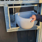 Close-up of a feeding trough being held in place on a horse stall, showing the attachment mechanism.