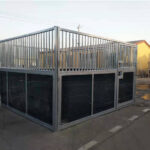 Another view of a metal horse stall with a sliding door and dark panels at the bottom, set against the backdrop of a storage area.