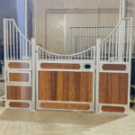 A horse stall door made of metal and wood, featuring an arch design at the top with a combination of solid wood panels and mesh, providing both security and ventilation.