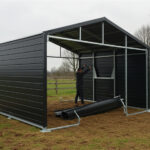 A black horse shelter with a metal frame and solid panels, under construction in a grassy area, with building materials scattered around.