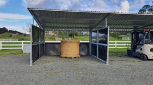 Completed portable horse shelter with a hay bale inside, set against a green landscape.