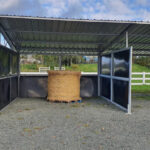 Portable horse stable with galvanized steel frame and HDPE panels featuring covered hay storage area and modular design on gravel foundation.