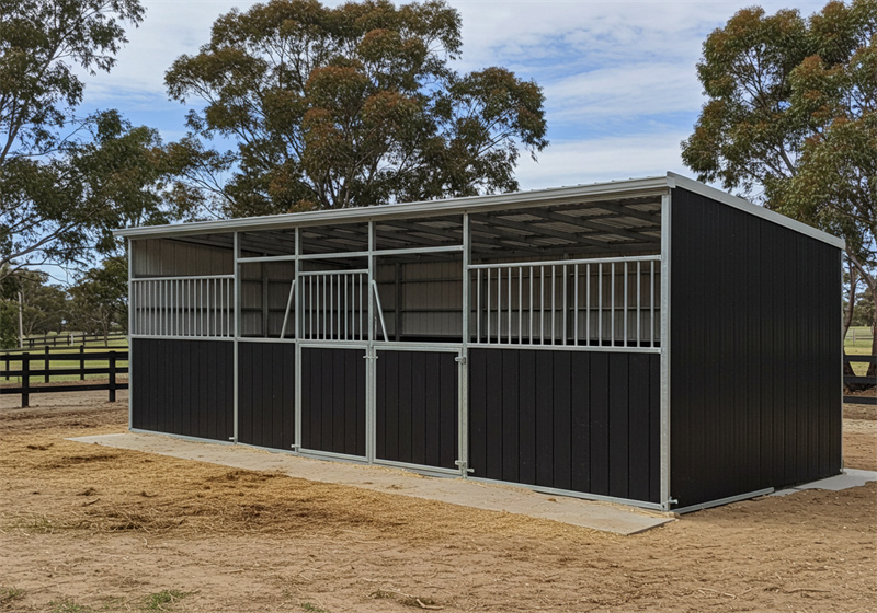 A three-stall DIY horse stable kit with dark brown lower panels and grey metal upper sections and roof. The stalls feature metal bars and gates, and the stable is built on a concrete foundation with straw scattered around it.