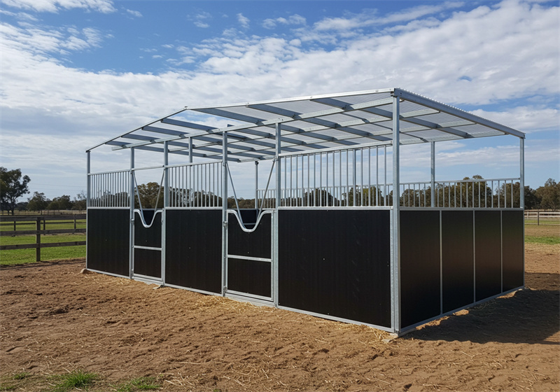 A three-stall DIY horse stable kit with dark brown lower panels, metal bar upper sections, and a translucent corrugated plastic roof. Each stall has a metal gate and a V-shaped opening for the horse's head. The stable is on a dirt and straw base.